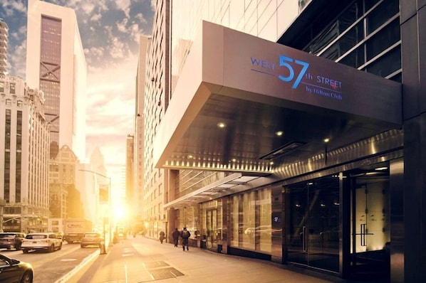 Un hôtel moderne, reconnaissable à son grand panneau indiquant « West 57th Street », à ses larges fenêtres et à sa façade en verre.