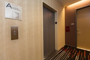 An elevator with a sign indicating use of stairs in case of fire, a door with a number plate, and a carpeted floor.
