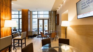 A hotel lobby with a glass table, chairs, a reception desk, and a large screen displaying Medicare information. - New York City | Midtown Escape | Near Central Park & Broadway (New York)