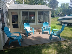 A covered outdoor deck with four blue Adirondack chairs, a small table, and a windowed enclosure.