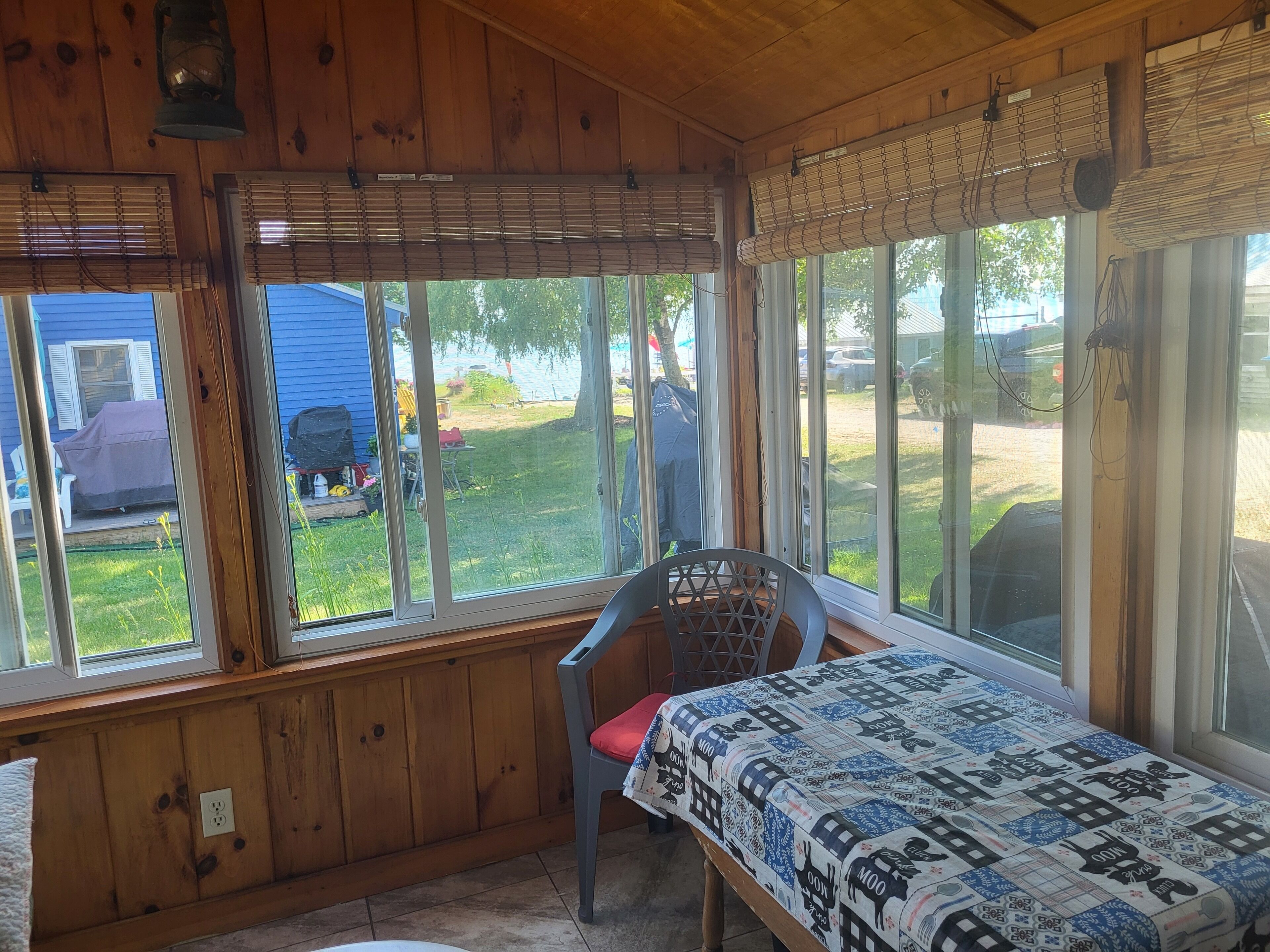 A wooden cabin with a bed, a chair, and large windows overlooking a yard.