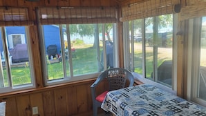 Une cabane en bois avec un lit, une chaise et de grandes fenêtres donnant sur une cour.