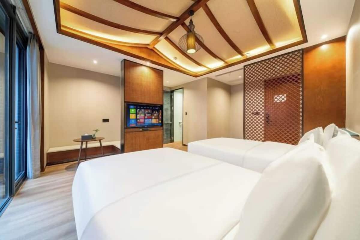 Habitación de hotel con dos camas, televisión, una mesita y un separador decorativo.