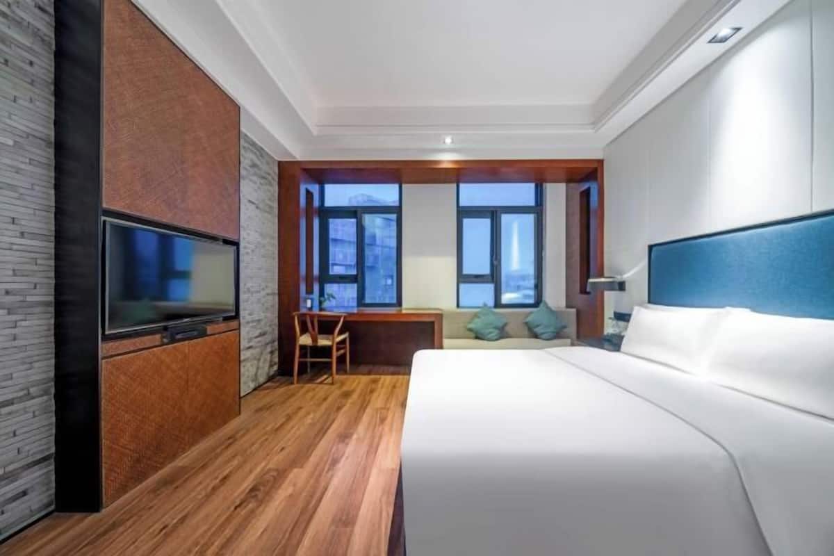 Una habitación de hotel con cama, escritorio, silla, televisión y ventanas amplias.