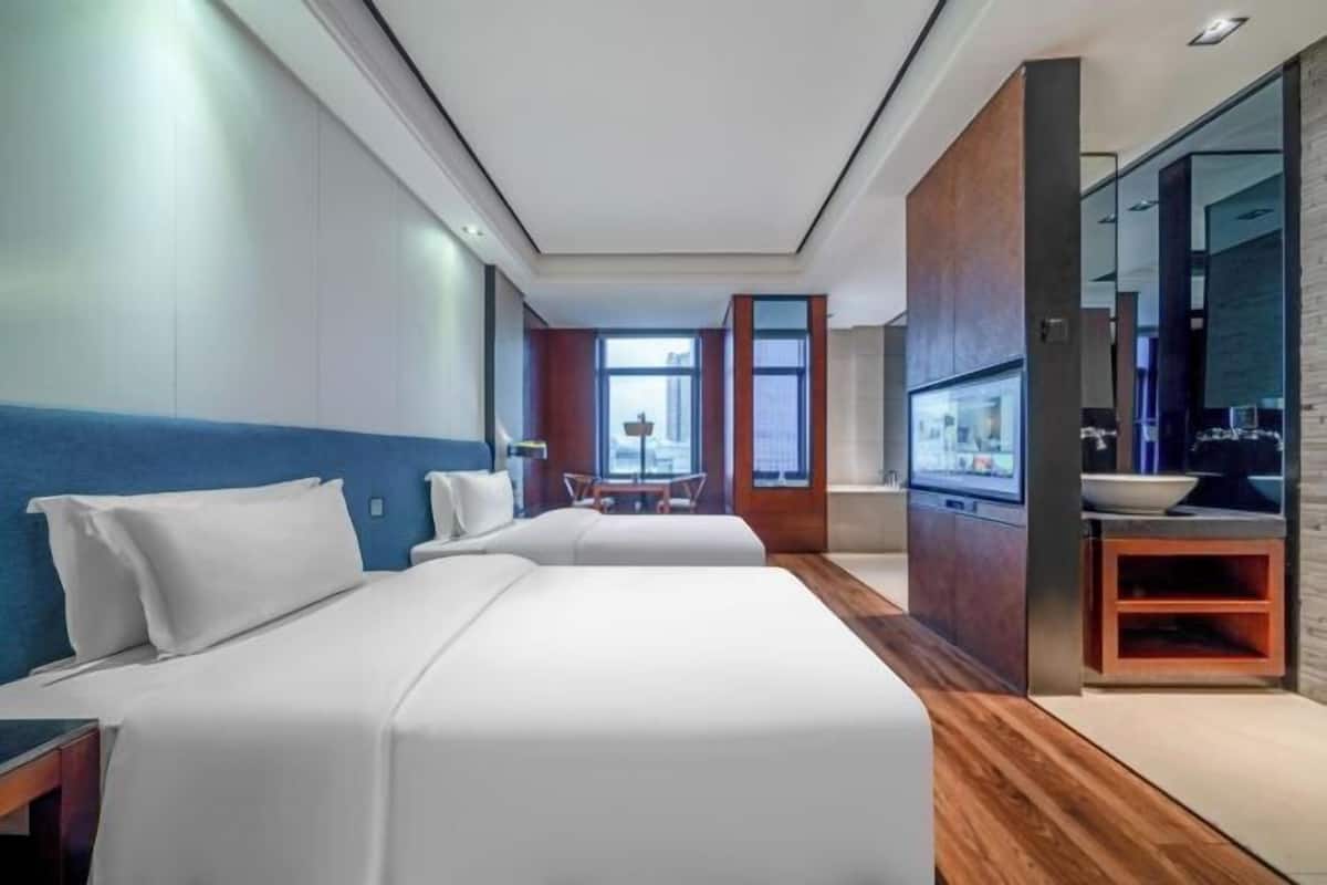 Una habitación de hotel moderna con dos camas, un panel de madera decorativo, un espejo grande y un televisor.