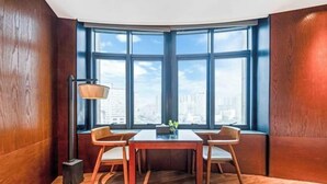 A corner room with a wooden floor, a table with chairs, a lamp, and a view of the city through large windows. - THE PULI HOTEL (Hangzhou)