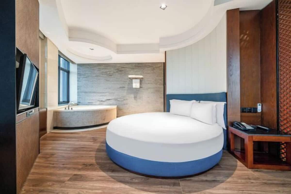 Un dormitorio moderno con una cama redonda, una bañera empotrada y suelo de madera.