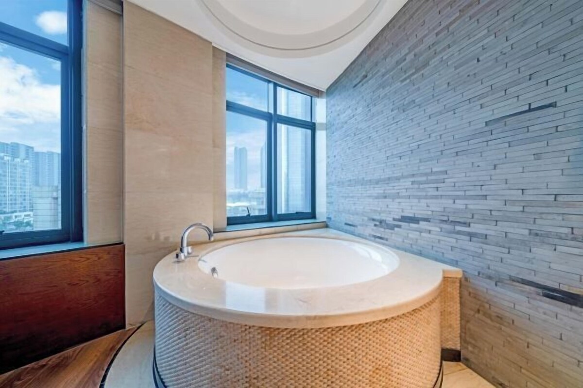 A modern bathroom with a freestanding bathtub, large windows, and a brick wall.