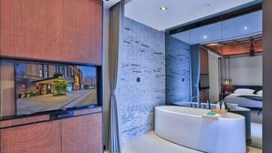 A modern hotel room with a large TV, a curved white bathtub, and a brick-patterned wall. - THE PULI HOTEL (Hangzhou)