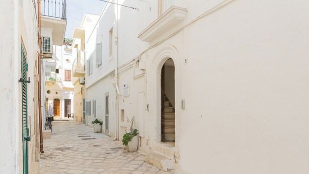 A narrow cobblestone street flanked by white buildings with balconies and shutters. - Residenza Vico Recupero by Wonderful Italy (Polignano a Mare)