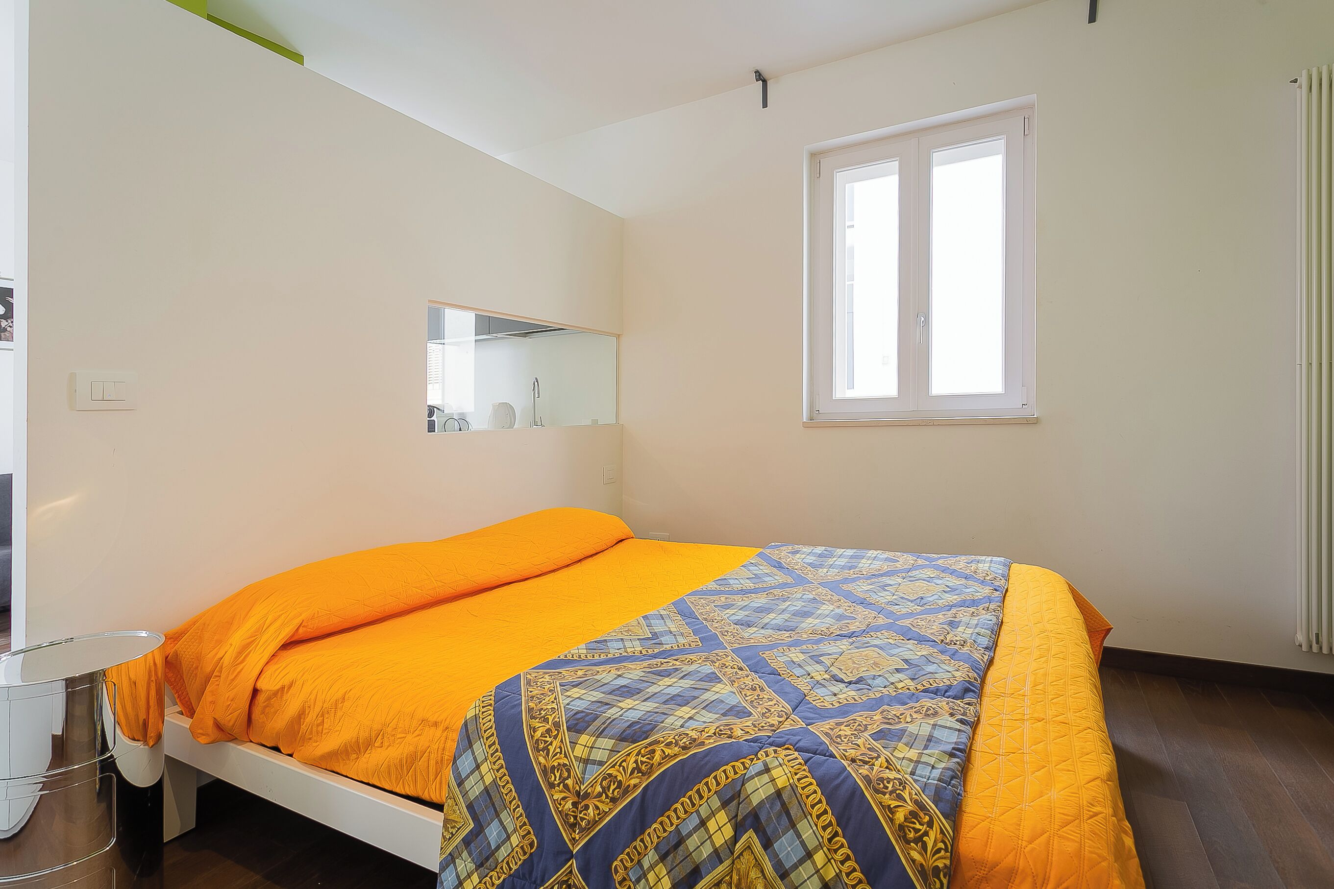 Een bed met een gebedruid sprei, een nachtkastje, een spiegel en een raam met gordijnen.