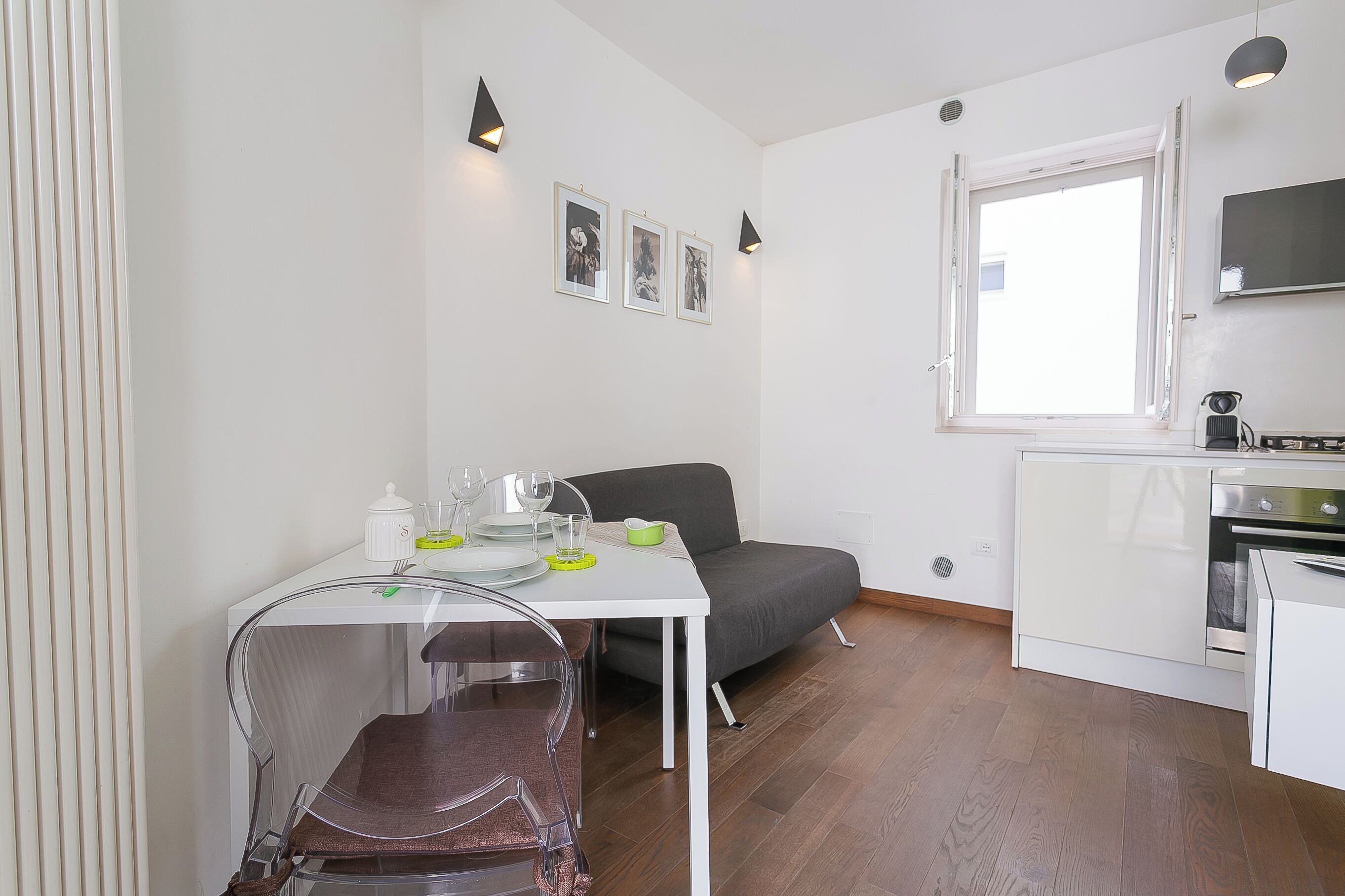 A compact kitchen with white cabinets, a dining table with chairs, a sofa, and a window.