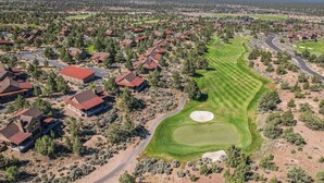 An aerial view of a residential area with houses, a golf course, and a mountain range in the background. - Cabin 75 Brasada Ranch + Hot Tub and Golf (Powell Butte)