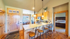 A spacious kitchen with wooden cabinets, a granite countertop, and a central island with bar stools. - Cabin 75 Brasada Ranch + Hot Tub and Golf (Powell Butte)
