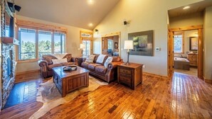 A spacious living room with wooden flooring, leather sofas, and a stone fireplace. - Cabin 75 Brasada Ranch + Hot Tub and Golf (Powell Butte)