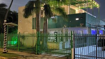 Una propiedad cercada con un espacio exterior cubierto, palmeras y un edificio de techo plano.