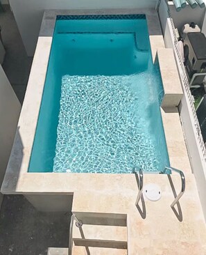 Una piscina rectangular con agua cristalina, rodeada por un solado de azulejos y una escalera metálica.
