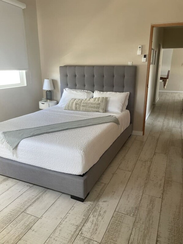 Un dormitorio moderno con una cama grande, una mesita de noche, una lámpara y vistas a un pasillo.