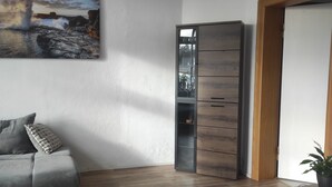 Ett vardagsrum med en grå soffa, ett träskåp och en målning som föreställer ett bergigt landskap.