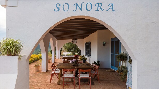 Patio esterno con tavolo e sedie, circondato da muri e archi bianchi, con la scritta 'SONORA' in alto.