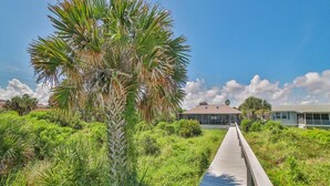 A wooden boardwalk leading to a building with a flat roof, surrounded by lush greenery and a clear sky. - Direct Oceanfront ~ Private Walkway ~ Excellent Rates! (Saint Augustine)