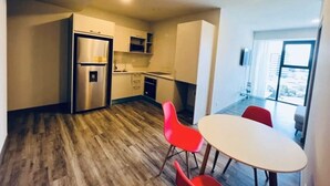 Una cocina moderna con refrigerador de acero inoxidable, piso de madera y un comedor con mesa blanca y sillas rojas.