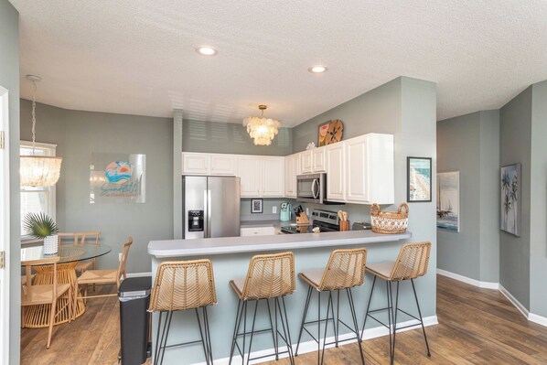 A modern kitchen with white cabinets, a central island with bar stools, and a chandelier. - Walk to Beach & Pool, Resort Amenities, Pvt Deck (Corolla)