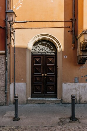 Une porte marron surmontée d’une fenêtre décorative en verre, flanquée de deux bornes et un lampadaire situé à gauche.