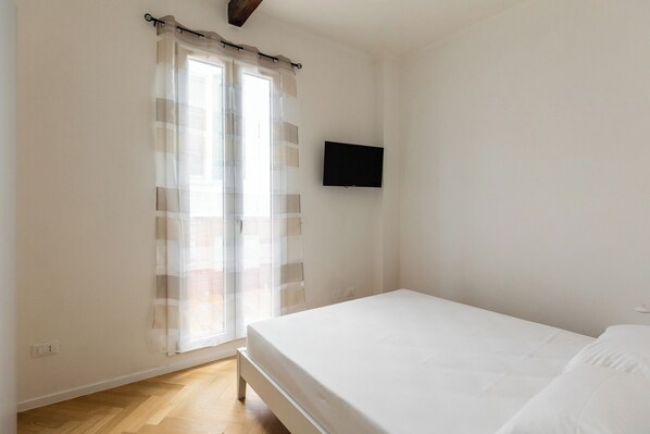 A bedroom with a bed, a television mounted on the wall, and a window with curtains. - Appartamento al Ghetto Ebraico by Wonderful Italy (Bologna)