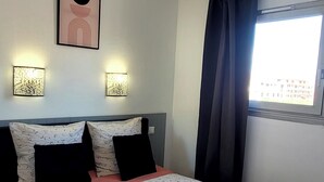Een net opgemaakt bed met bloemenbeddengoed, twee wandlampen en een raam met gordijnen.