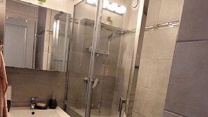 Een moderne badkamer met een douchecabine van glas, een wastafel met spiegel erboven, en een kleine potplant op het aanrecht.