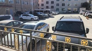 A parking lot with multiple cars and buses, surrounded by buildings with multiple windows and balconies.