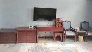 A room with a flat-screen TV mounted on the wall, a wooden desk with a chair, and a small table with a chair.