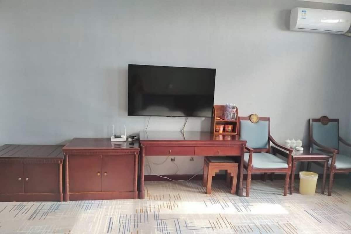 A room with a flat-screen TV mounted on the wall, a wooden desk with a chair, and a small table with a chair.