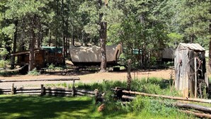 Un terrain de camping rustique avec un chariot couvert, des cabanes en bois et une petite construction en bois.