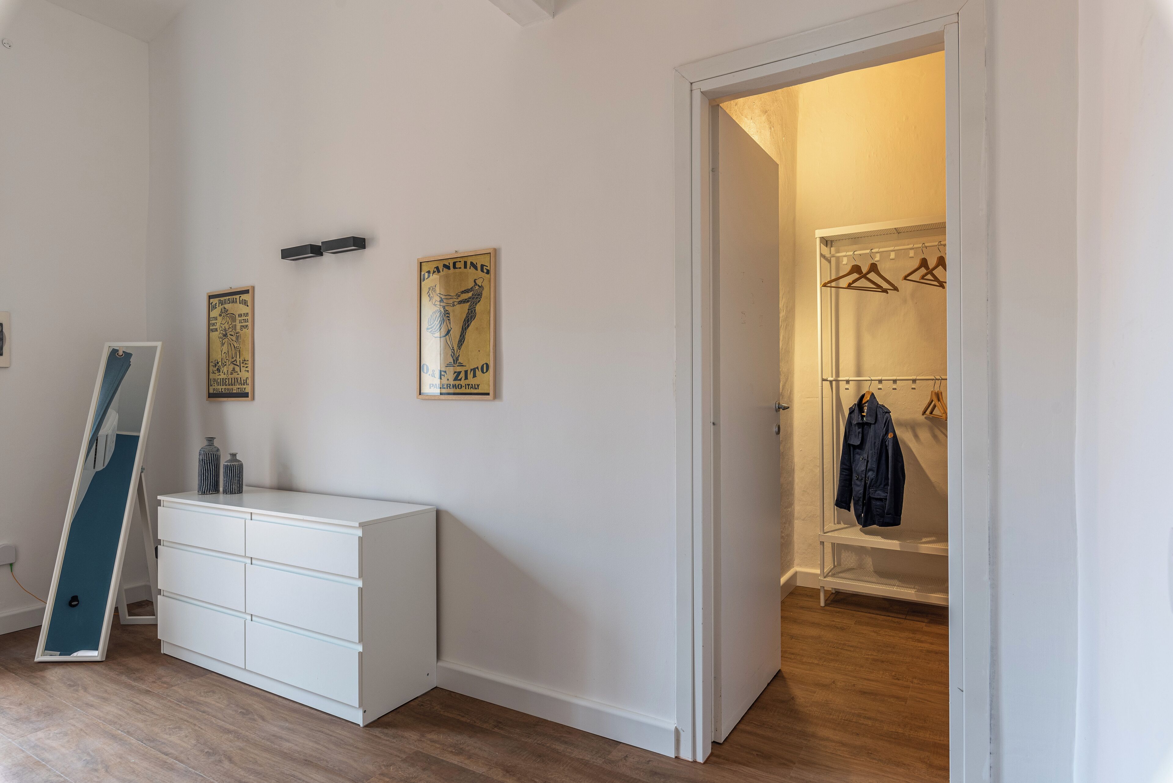 Ein Zimmer mit einem weißen Schminktisch, einem blauen Klappstuhl und einem Kleiderschrank mit Kleidung.