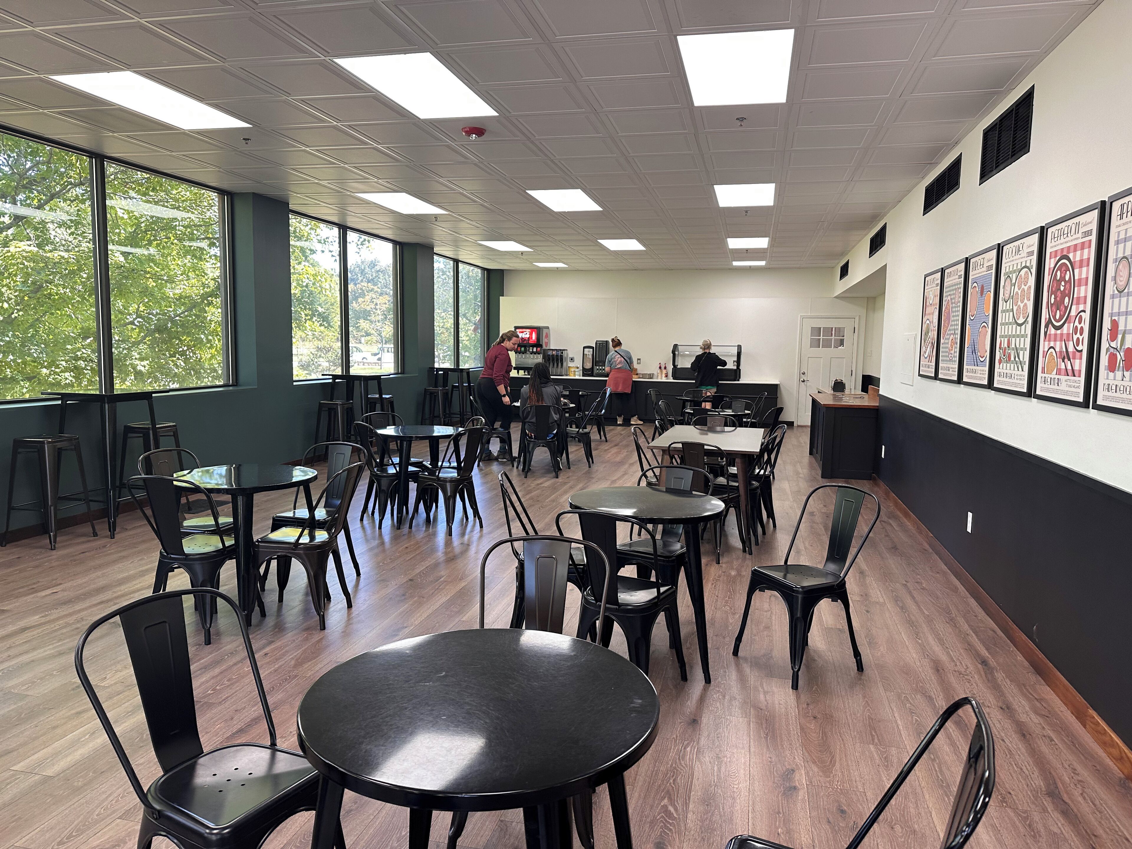 A spacious indoor dining area with multiple tables and chairs, large windows, and a counter with staff.
