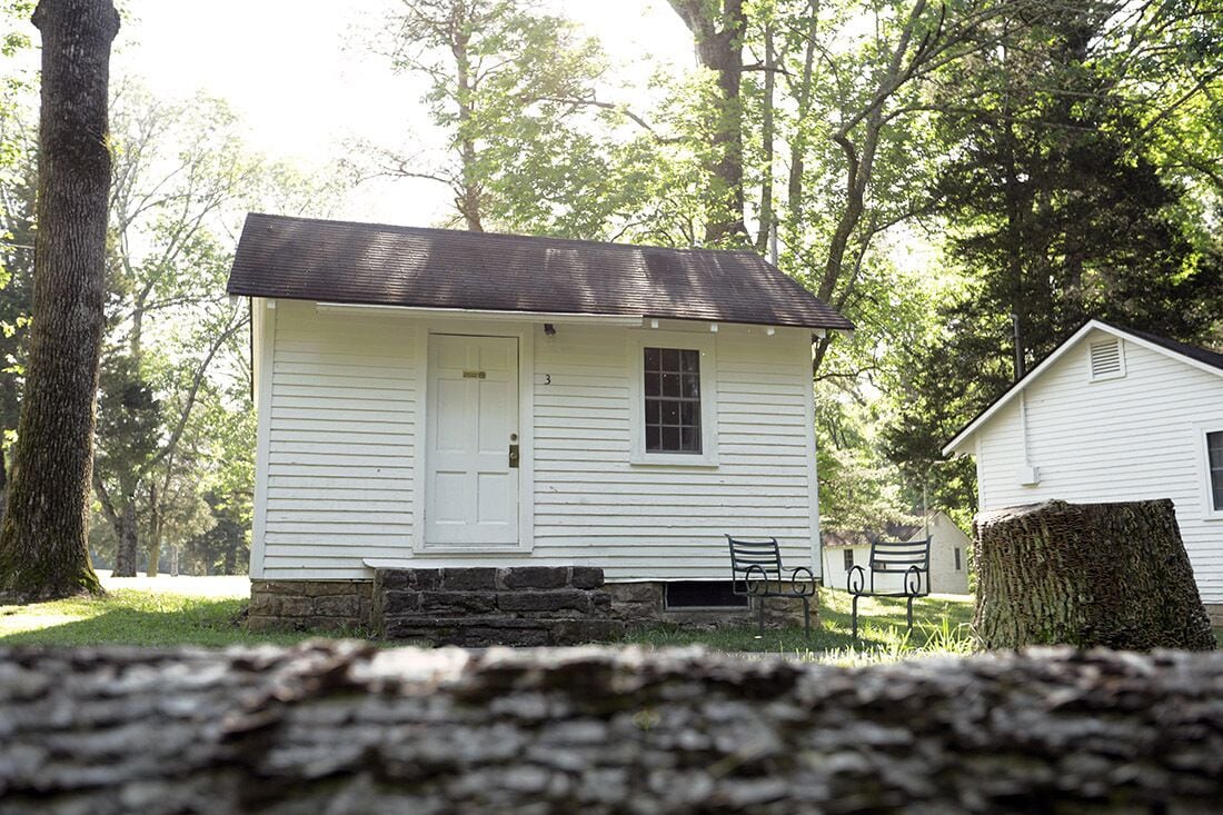 A small white cabin with a door and window, surrounded by trees.