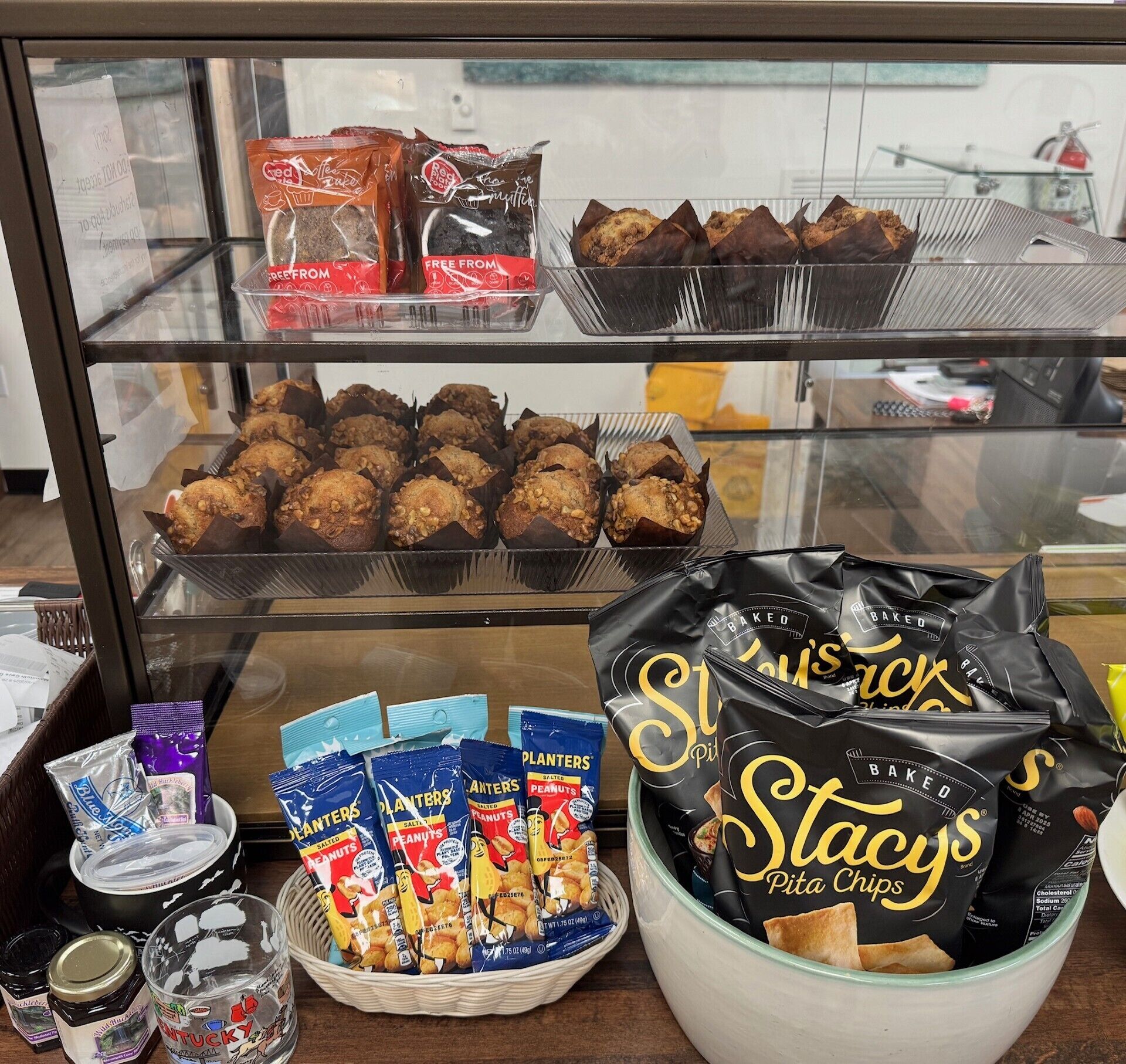 Una vitrina con productos de panadería y snacks, incluyendo muffins, galletas y chips de pita.