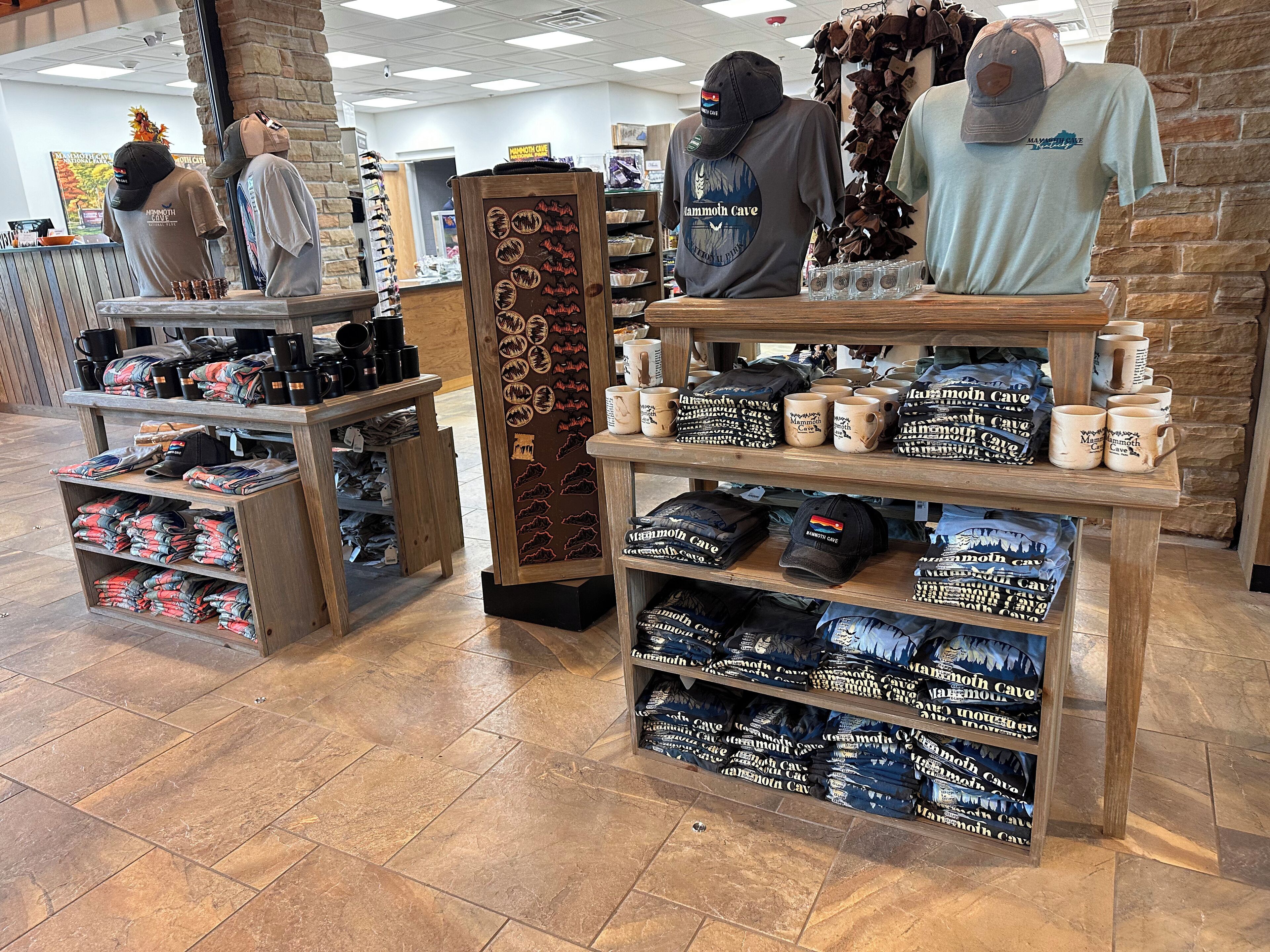 Loja comercial com prateleiras de madeira repletas de produtos, incluindo chapéus e bolsas, e uma placa indicando o tema 'Mammoth Cave'.