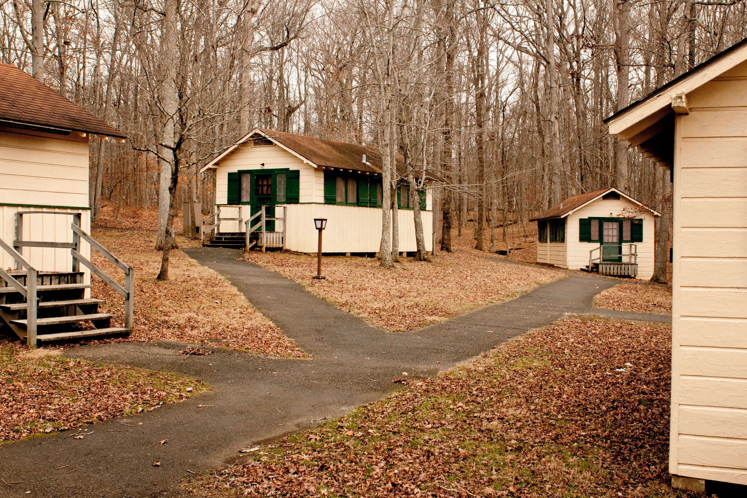 A row of small, single-story cabins with green shutters, a central path leading to the main cabin, and a wooded backdrop.