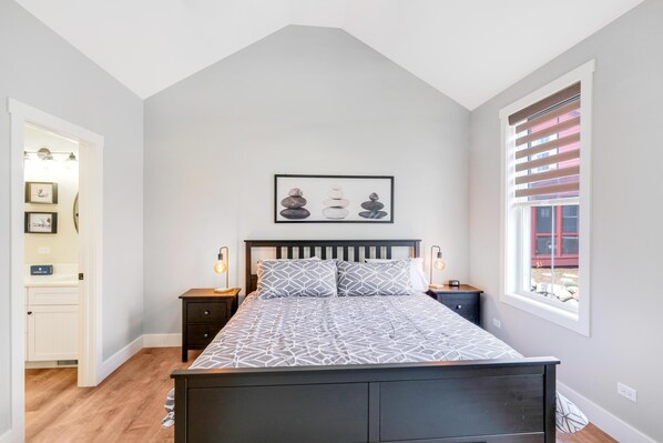 Une chambre à coucher avec un lit, des tables de chevet, une fenêtre avec des stores et un tableau encadré au mur.