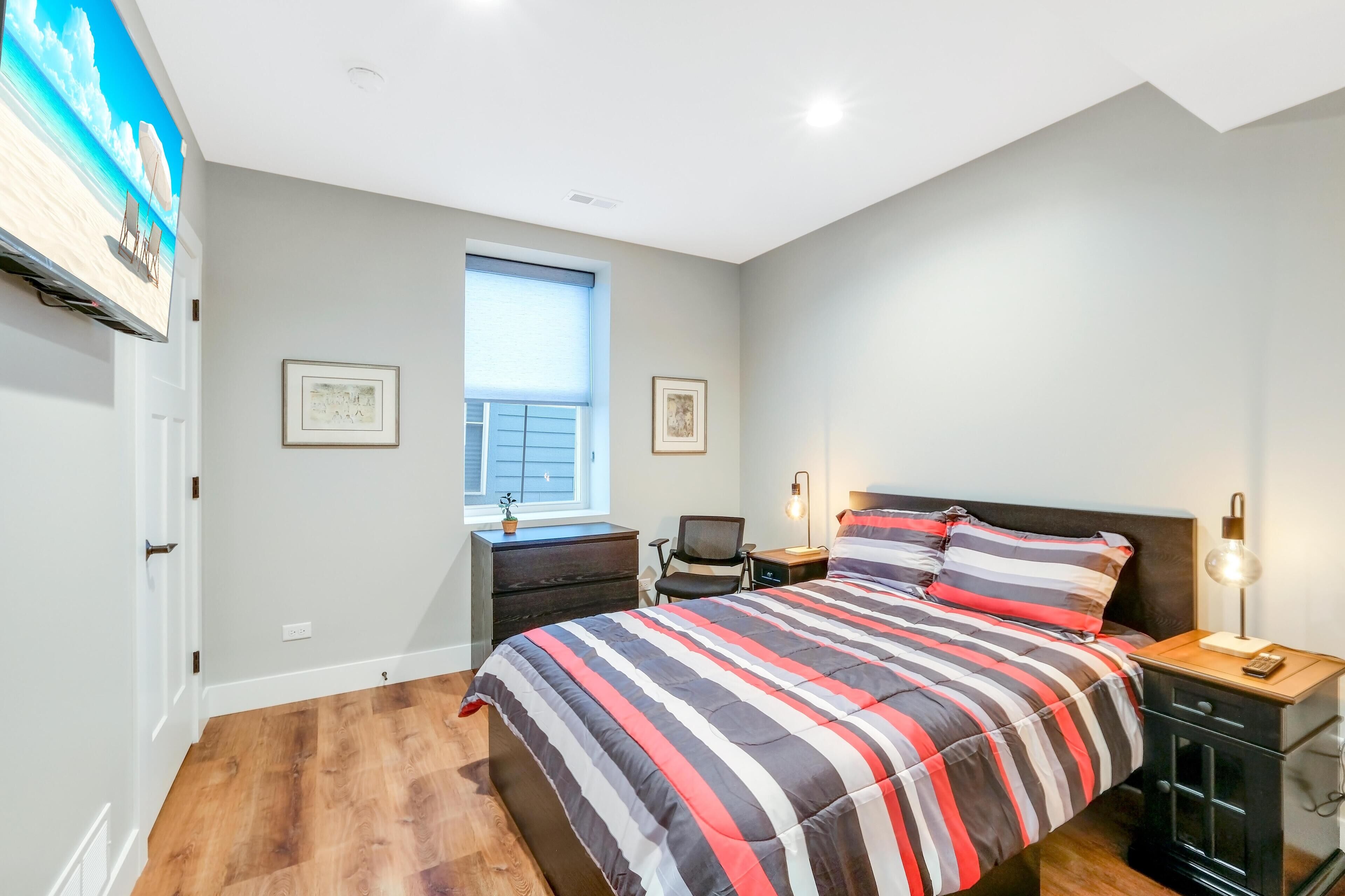 A bedroom with a bed, bedside tables, a desk, a chair, and a window.