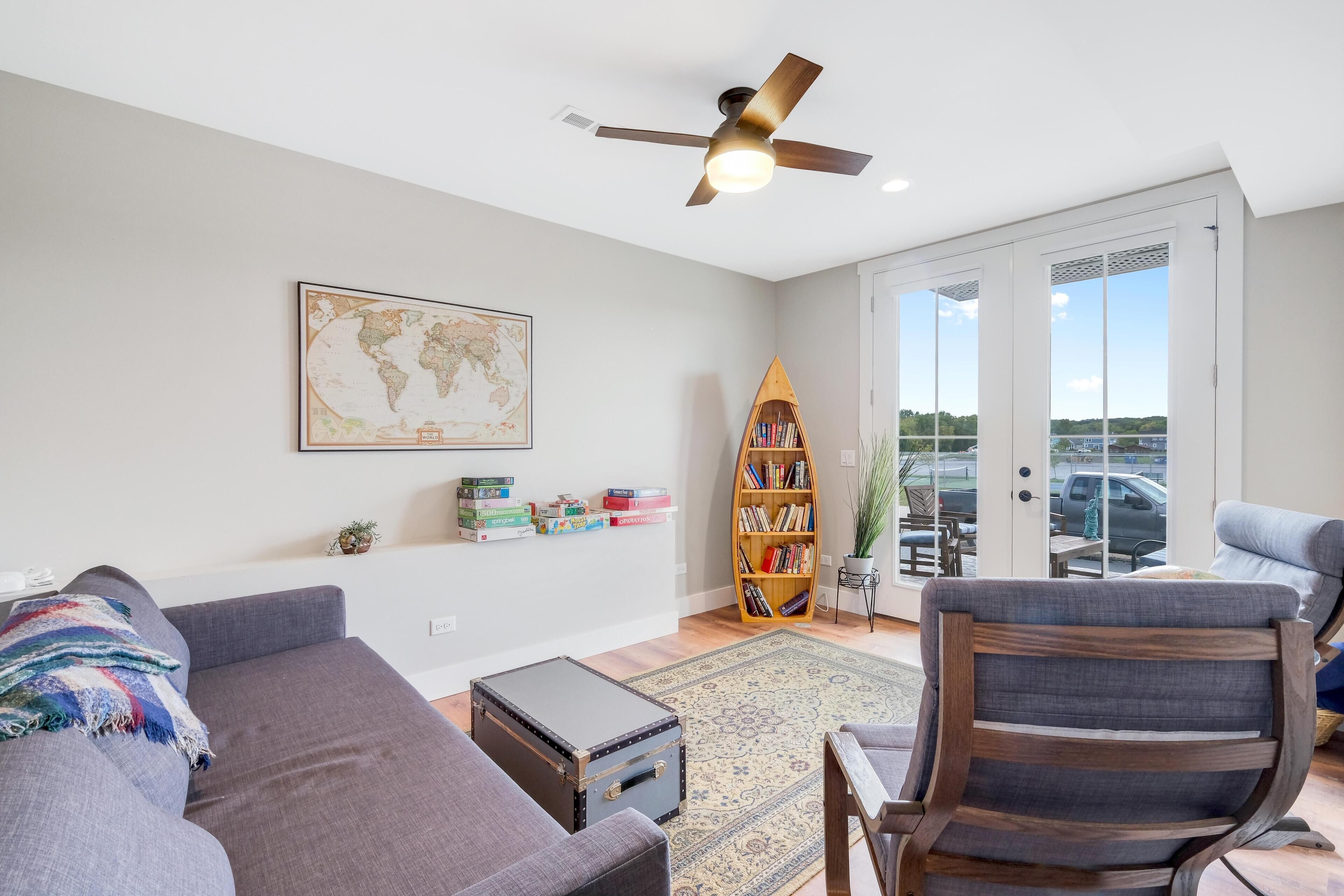 A living room with a gray sofa, a wooden chair, a globe map on the wall, a bookshelf, and a suitcase.