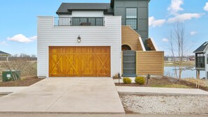 A modern two-story house with a large garage, a balcony, and a view of a lake. - La Dolce Vita (Ottawa)