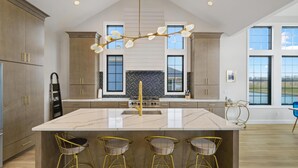 A modern kitchen with a large island, bar stools, and a unique chandelier. - La Dolce Vita (Ottawa)