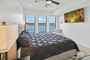 A bedroom with a large bed, a ceiling fan, and a view of a lake through large windows. - La Dolce Vita (Ottawa)