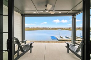 A covered outdoor area with two Adirondack chairs, a ceiling fan, and a view of a body of water with docks. - La Dolce Vita (Ottawa)