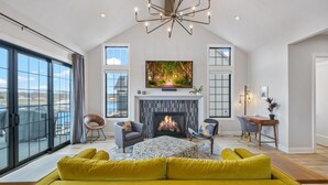 A spacious living room with a fireplace, large windows, and a modern chandelier. - La Dolce Vita (Ottawa)