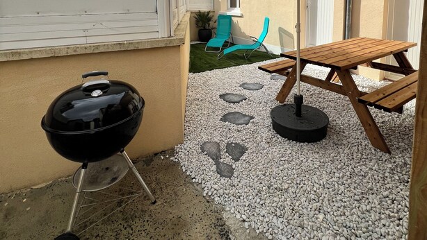 A patio area with a barbecue grill, a wooden table, and a blue chair. - Charming house with garden, harbour view, beach within walking distance (Dives-sur-Mer)